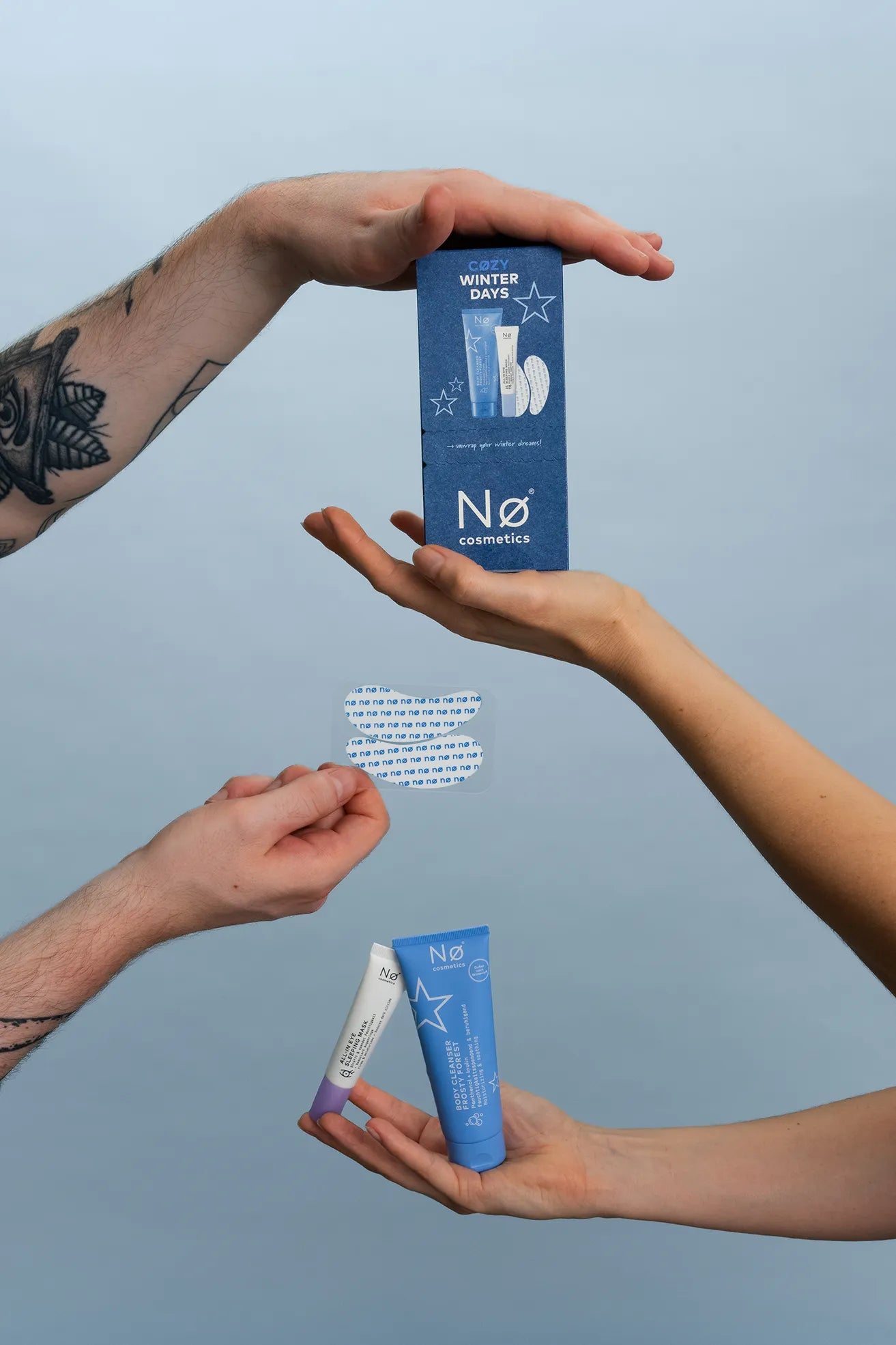 Vier Hände halten Winter-Edition-Produkte von Nø Cosmetics aus 2026 vor blauem Hintergrund hoch.