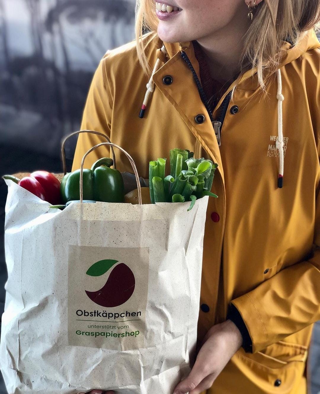 Eine junge Frau hält eine Tüte von Obstkaeppchen in den Händen, die mit Gemüse gefüllt ist.