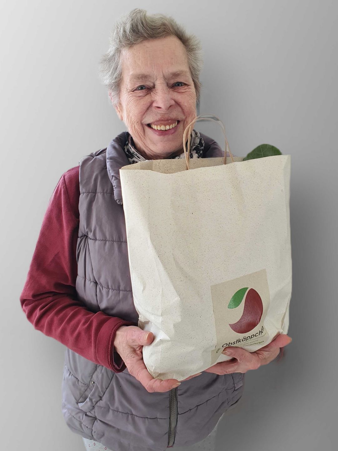 Eine Seniorin hält lächelnd ihre Tüte von Obstkaeppchen in die Kamera.