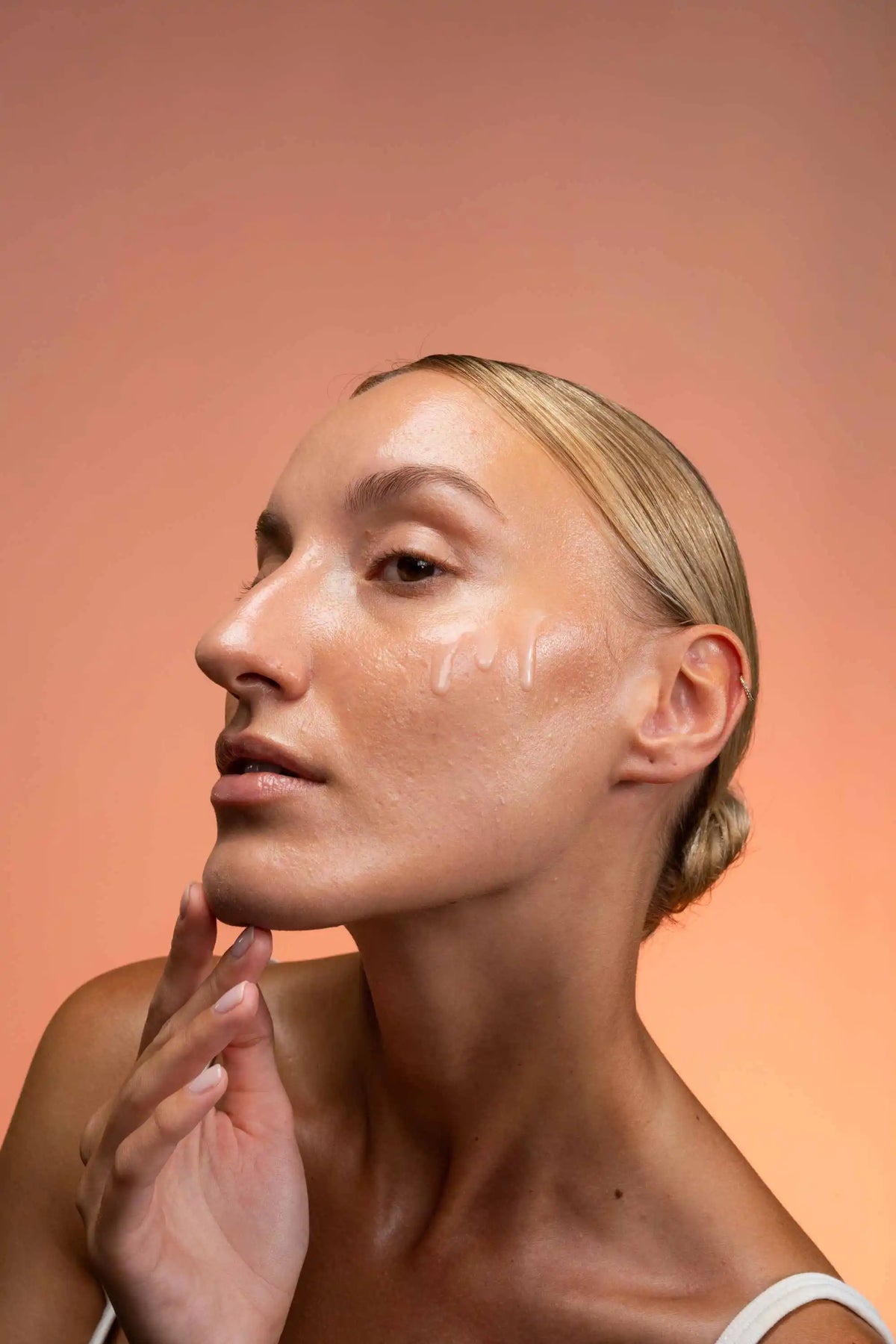 Frau mit sichtbarer Skincare-Textur auf der Wange vor orangefarbenem Hintergrund.